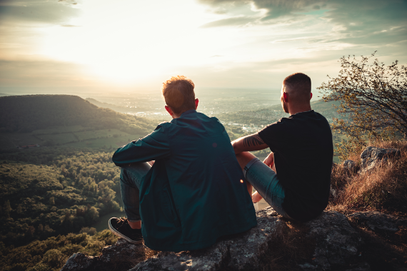 Zwei Männer sitzen nebeneinander und schaue sich den Sonnenuntergang an. 