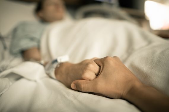 Zwei Hände, die sich am Krankenbett umklammern.